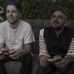 Photo of two men on a sofa holding video game controlers.